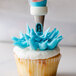 A person uses an Ateco chrysanthemum piping tip to pipe blue frosting onto a cupcake.