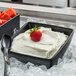 A G.E.T. Enterprises Bugambilia square metal bowl with black textured finish filled with white cream and a strawberry on top.