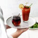 A person holding a tray with a glass of brown liquid and a glass of red liquid on an American Metalcraft clear non skid tray.