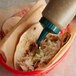 A person using a Vollrath Traex squeeze bottle to pour sauce on a tortilla in a basket.