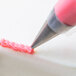 A close up of a Ateco Closed Star piping tip being used to pipe pink frosting.