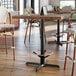 A Lancaster Table & Seating black cast iron bar height table base with a foot ring on a table in a restaurant dining area.