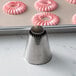 A metal Ateco Sultan protruding cone piping tip with pink frosting on it.
