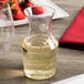 A clear plastic disposable wine carafe filled with white wine.