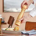 A person holding an Acopa wooden pepper mill over a plate of food.