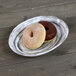 An Elite Global Solutions black oval melamine plate with two donuts on it on a wood table.