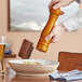 A person using an Acopa brown wooden pepper mill to add salt to a bowl of food.