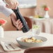 A hand using an Acopa matte black wooden pepper mill to season a bowl of pasta.