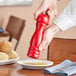 A person using an Acopa red wooden pepper mill to add spices to food.