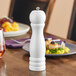 An Acopa white wooden pepper mill on a table.