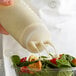 A person using a Vollrath Tri Tip squeeze bottle to pour dressing onto a salad.