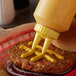 A person using a yellow Vollrath Twin Tip squeeze bottle to put mustard on a burger.