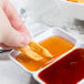 A hand holding a piece of food over a white GET Water Lily sauce dish.