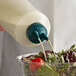 A person using a Vollrath Twin Tip Squeeze Bottle to pour dressing onto a salad.