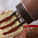 A person using a Vollrath Tri Tip bottle cap to put ketchup on a hamburger bun.