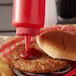 A burger with a red squeeze bottle of ketchup and fries served in a basket.