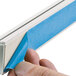 A person's hand using a blue tape to attach a white D-Line decorative cord cover.