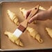 A person using a Carlisle Sparta Spectrum pastry brush to baste croissants.