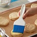 A hand holding a Carlisle Sparta Spectrum pastry brush over a tray of biscuits.