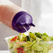 A person pouring purple liquid from a Vollrath Tri Tip squeeze bottle with a purple cap onto a salad.