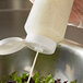 A hand using a white Vollrath squeeze bottle to pour dressing onto a salad.