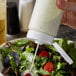 A person using a Vollrath Clear Squeeze Bottle to pour dressing onto a salad.