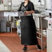 A woman in a black Choice vinyl dishwasher apron holding a tray.