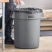 A man standing next to a Lavex gray commercial trash can in a professional kitchen.