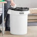 A man putting a black trash bag in a white Lavex round commercial trash can.