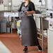 A woman wearing a Choice brown vinyl dishwasher apron holding a tray.