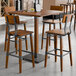 A square rustic walnut finish solid wood bar height table with four matching industrial-style bar stools.