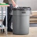 A man standing next to a Lavex gray round commercial trash can.