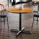 A round standard height table with a reversible walnut or oak top and a black cast iron base.