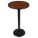 A Lancaster Table & Seating bar height table with a round walnut and oak top on a black cast iron base.