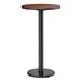 A round bar height table with a reversible walnut and oak top and a black cast iron base.