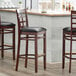 Three Lancaster Table & Seating mahogany wood window back bar stools with black vinyl seats at a counter.