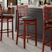 A Lancaster Table & Seating mahogany wood bar stool with a black vinyl cushion.
