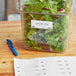 A container of green salad with Cambro dissolvable labels and a pen on a table.