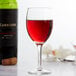 A Libbey wine glass filled with red wine on a table next to a bottle of wine.