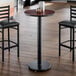 A round bar height table with a reversible cherry and black top and a cast iron base.