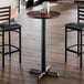 A round bar height table with a reversible cherry and black top and a cast iron base.