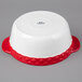 A white Tuxton round china casserole dish with red band and handles.