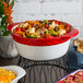 A Tuxton round red and white casserole dish filled with food on a table.