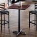A square bar-height table with a reversible cherry and black top, supported by a black cast iron base.