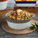 A Tuxton round black truffle band casserole dish filled with food on a table.