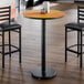 A round bar height table with a reversible walnut and oak top and a black cast iron base.