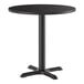 A round black standard height table with a single central pedestal and a four-pronged cast iron base.