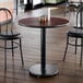 A round standard height table with a reversible cherry and black top and a 17-inch cast iron base, shown in a restaurant setting.