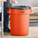 A man pushing a Lavex orange trash can with a black bag inside.
