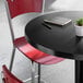 A round black table with a cast iron base, accompanied by red chairs, a notebook, a pen, and a small potted plant on top.